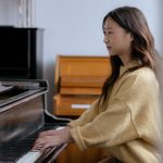 Side view of Asian woman in casual clothes practicing music on piano while sitting in bright classroom