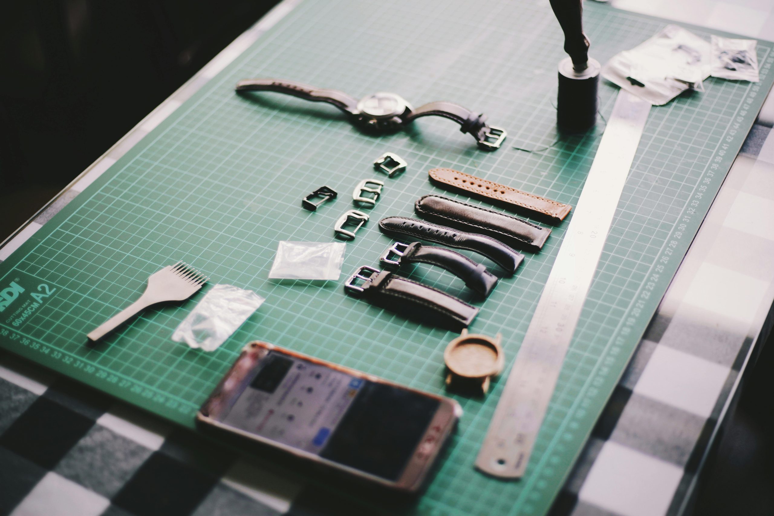 Close-up of watchmaking tools and leather straps on a crafting table.